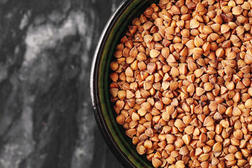 Buckwheat groats in green bowl. Healthy gluten free food. Natural plant-based grain. Rustic table closeup view. Simple vegan nutrition.