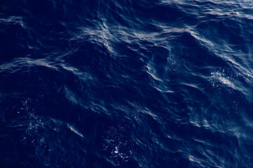 A top-down view of waves and the foam wake created by a moving ship. The deep blue and white tones create a striking contrast, capturing the energy of the sea