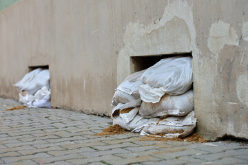 Sandbags stacked to block basement air vents in building wall to prevent flooding. Emergency flood protection during heavy rain or water rise