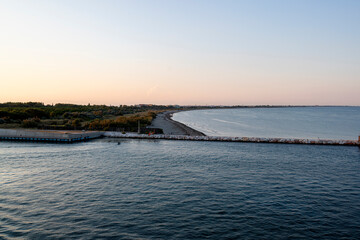 Fototapeta premium A breathtaking sunset over the Venetian waters, highlighting a lighthouse and the silhouette of the coastline. The golden hues reflect beautifully on the rippling waves