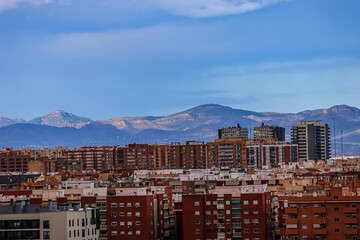 Brown houses in spanish town with mountains on horizon under blue sky	
