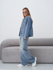 A young woman stands confidently in a stylish oversized denim jacket and loose jeans, wearing...