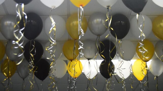 Globos grises, amarillos, platados, blancos y negros en el techo. El video enfoca y desenfoca.
