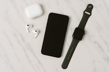 Top view of smart tech accessories including a smartphone, smartwatch, and wireless earbuds on a marble table..