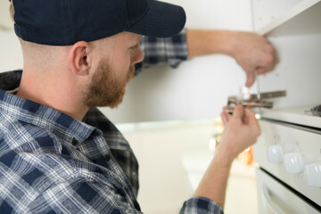 handyman fixing kitchen cabinet with screwdriver