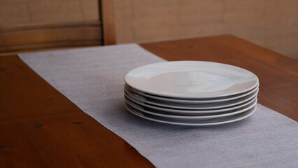 Stack of white plates on wooden table with linen runner