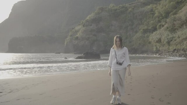 Woman smiling alone on beach with camera and sunlight on face (SLOG3)