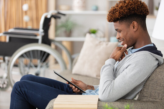 man relaxing on sofa with tablet near wheelchair