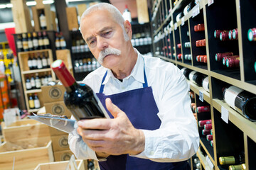smiling senior worker choosing wine at the supermarket