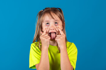 Happy funny young blonde girl posing, fooling around and showing tongue against blue background