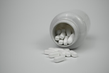 White pills tablets spilled from a bottle on a light grey background 