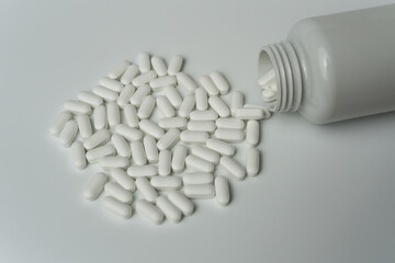 White pills tablets spilled from a bottle on a light grey background 