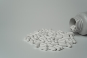 White pills tablets spilled from a bottle on a light grey background 