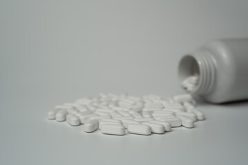 White pills tablets spilled from a bottle on a light grey background 