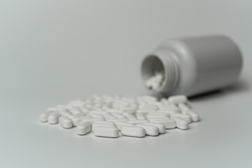 White pills tablets spilled from a bottle on a light grey background 