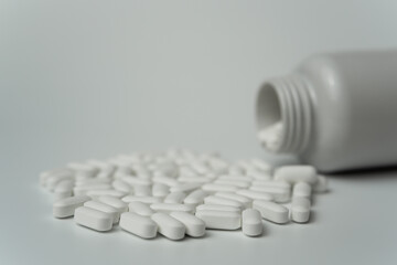 White pills tablets spilled from a bottle on a light grey background 