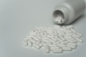 White pills tablets spilled from a bottle on a light grey background 