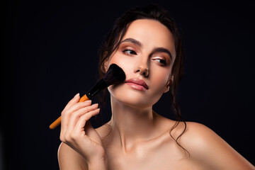 Portrait of a stylish young woman applying makeup with a brush against a dark background