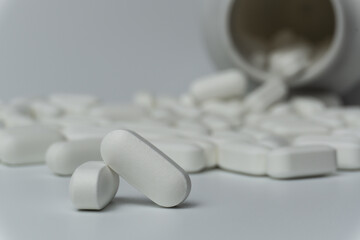 White pills tablets spilled from a bottle on a light grey background 