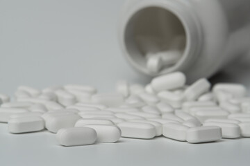 White pills tablets spilled from a bottle on a light grey background 