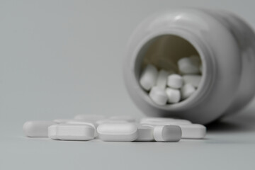 White pills tablets spilled from a bottle on a light grey background 