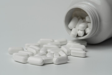 White pills tablets spilled from a bottle on a light grey background 