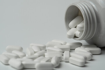White pills tablets spilled from a bottle on a light grey background close up