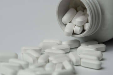 White pills tablets spilled from a bottle on a light grey background close up
