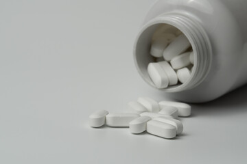 White pills tablets spilled from a bottle on a light grey background 