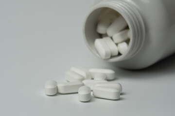 White pills tablets spilled from a bottle on a light grey background close up