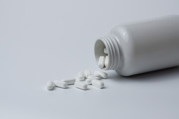 White pills tablets spilled from a bottle on a light grey background 