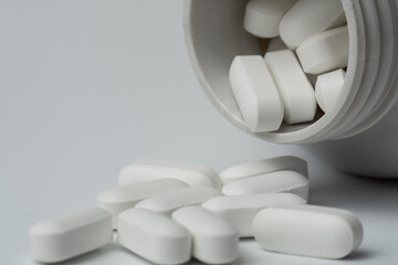 White pills tablets spilled from a bottle on a light grey background close up