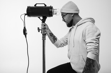 Smiling man in yellow hoodie holding professional lighting equipment in studio like microphone....