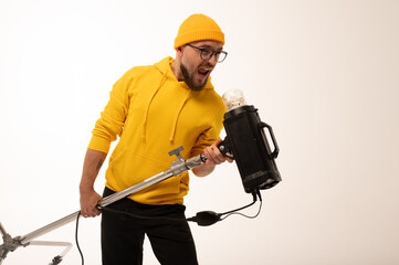 Smiling man in yellow hoodie holding professional lighting equipment in studio. Behind-the-scenes concept with cheerful crew member during photo or video shoot setup