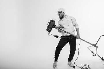 Smiling man in yellow hoodie holding professional lighting equipment in studio like microphone....