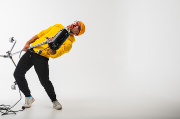 Smiling man in yellow hoodie holding professional lighting equipment in studio. Behind-the-scenes concept with cheerful crew member during photo or video shoot setup