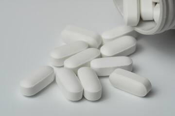 White pills tablets spilled from a bottle on a light grey background close up