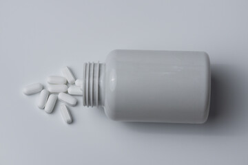 White pills spilled from a bottle on a light grey background top view