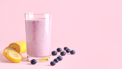 A tall glass filled with a pink smoothie surrounded by banana slices and berries.