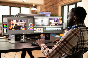 African american filmmaker working on a high quality video project, refining visuals and enhancing audio on his desktop monitors. Black man using advanced editing software in modern production office.
