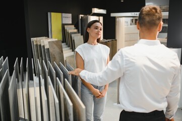 Obraz premium Salesman and a female customer choosing a right ceramic tile for her home, at the home design store