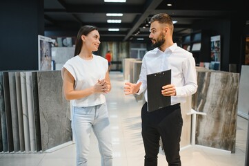 Young woman with sales man choosing tiles at building market