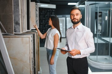Young woman with sales man choosing tiles at building market