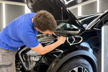 Process of paintless dent repair on car body. The mechanic at the auto shop with tools to repair dents in car body. Body repair. A specialist repairs a dent on the car body without painting. PDR. 