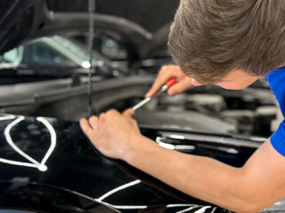 Process of paintless dent repair on car body. The mechanic at the auto shop with tools to repair dents in car body. Body repair. A specialist repairs a dent on the car body without painting. PDR. 