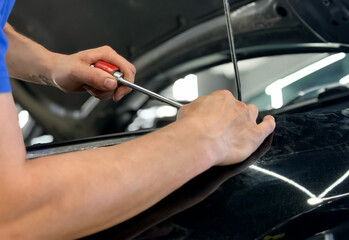 Process of paintless dent repair on car body. The mechanic at the auto shop with tools to repair...