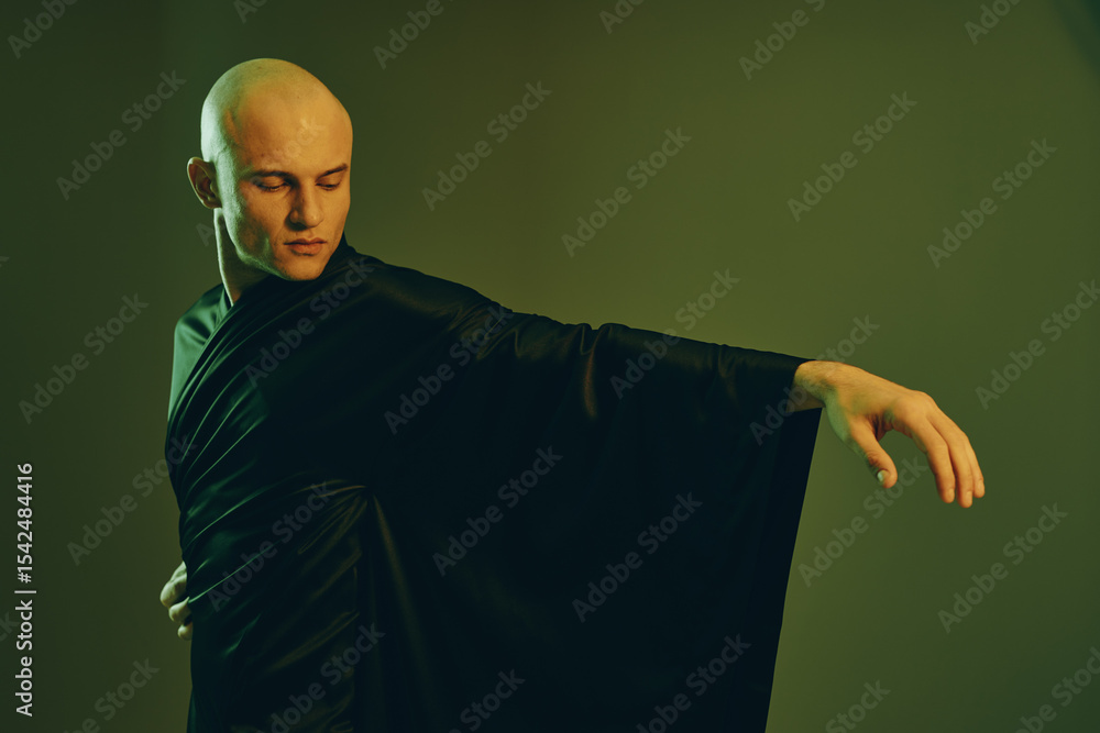 Poster elegant man in a flowing black robe with a serene expression, striking a graceful pose in soft, mute