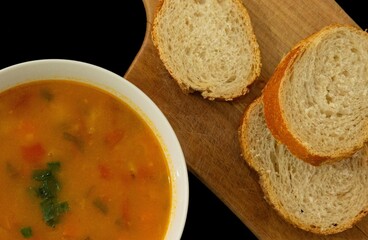Sopa de legumes com caldo amarelo e fatias de pão para acompanhar. 