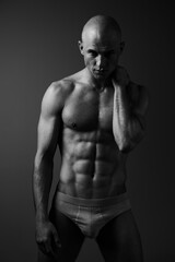 Fototapeta premium Black and white portrait of a muscular man conveying strength and confidence, showcasing his sculpted physique in dramatic lighting.