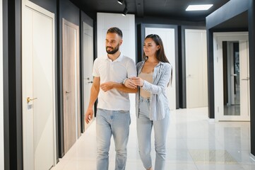 Portrait of smiling young man and woman shopping in the hardware store choosing different door...